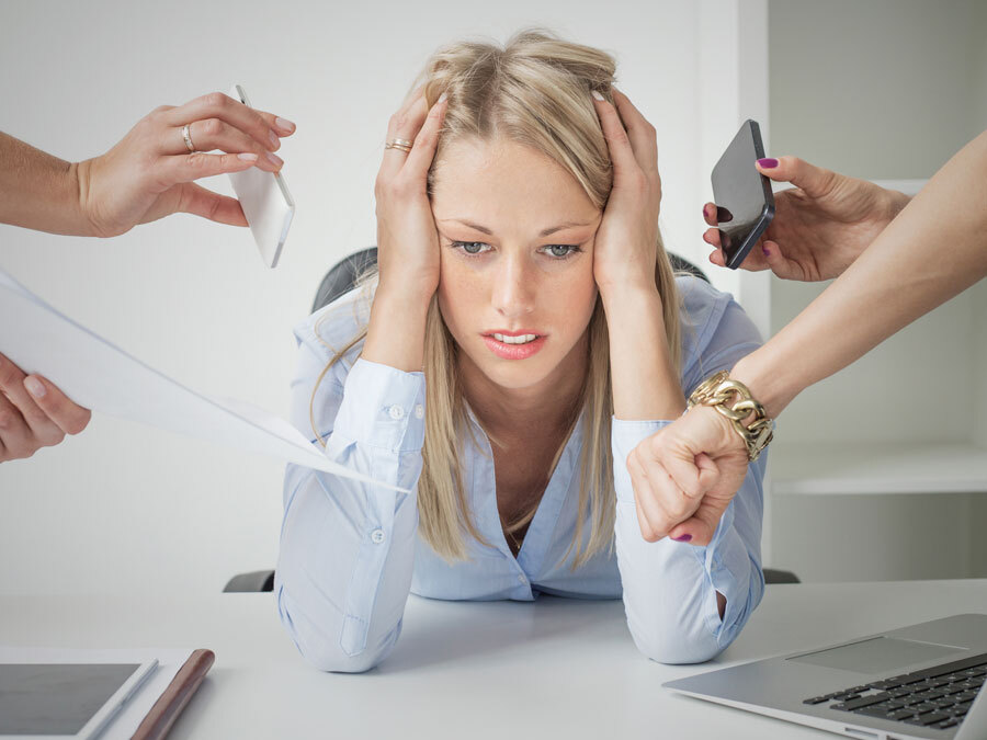Eine Frau an ihrem Arbeitsplatz. Sie hält sich den Kopf, weil sie überlastet ist. Sie hat einen Burnout am Arbeitsplatz.
